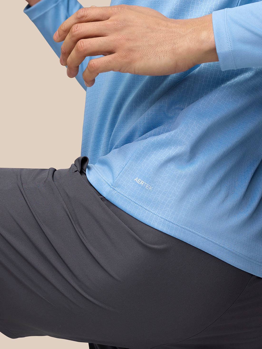 Close up of the lower back hem of sky blue Adapt Training 1/4 Zip Top with AERTEK branding.