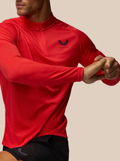 Man wearing red Adapt Training 1/4 Zip Top with raglan long sleeves, front zip and Castore logo on the left chest; all over print.