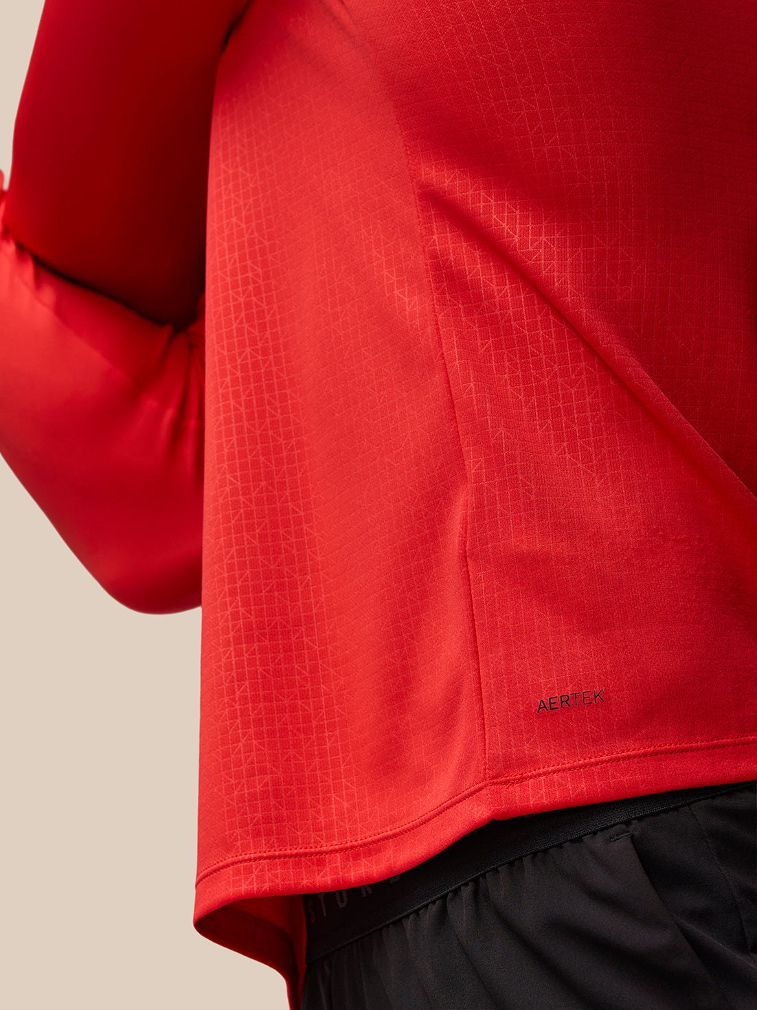 Close up of red Adapt Training top fabric showing AERTEK texture and hem seam
