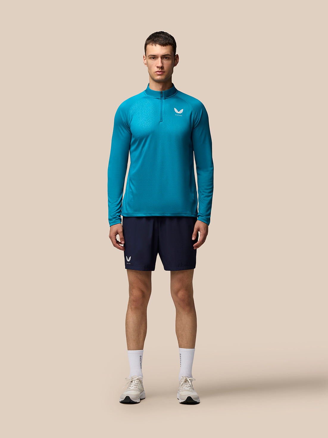 Male model wearing teal Adapt Print 1/4 Zip Top with geometric pattern and Castore branding