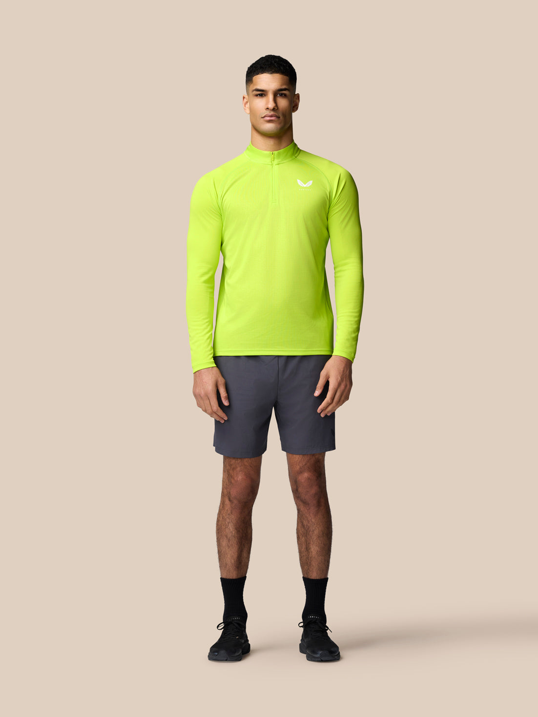 Full body shot of a man wearing neon lime Adapt Training 1/4 Zip top with long sleeves against a beige backdrop
