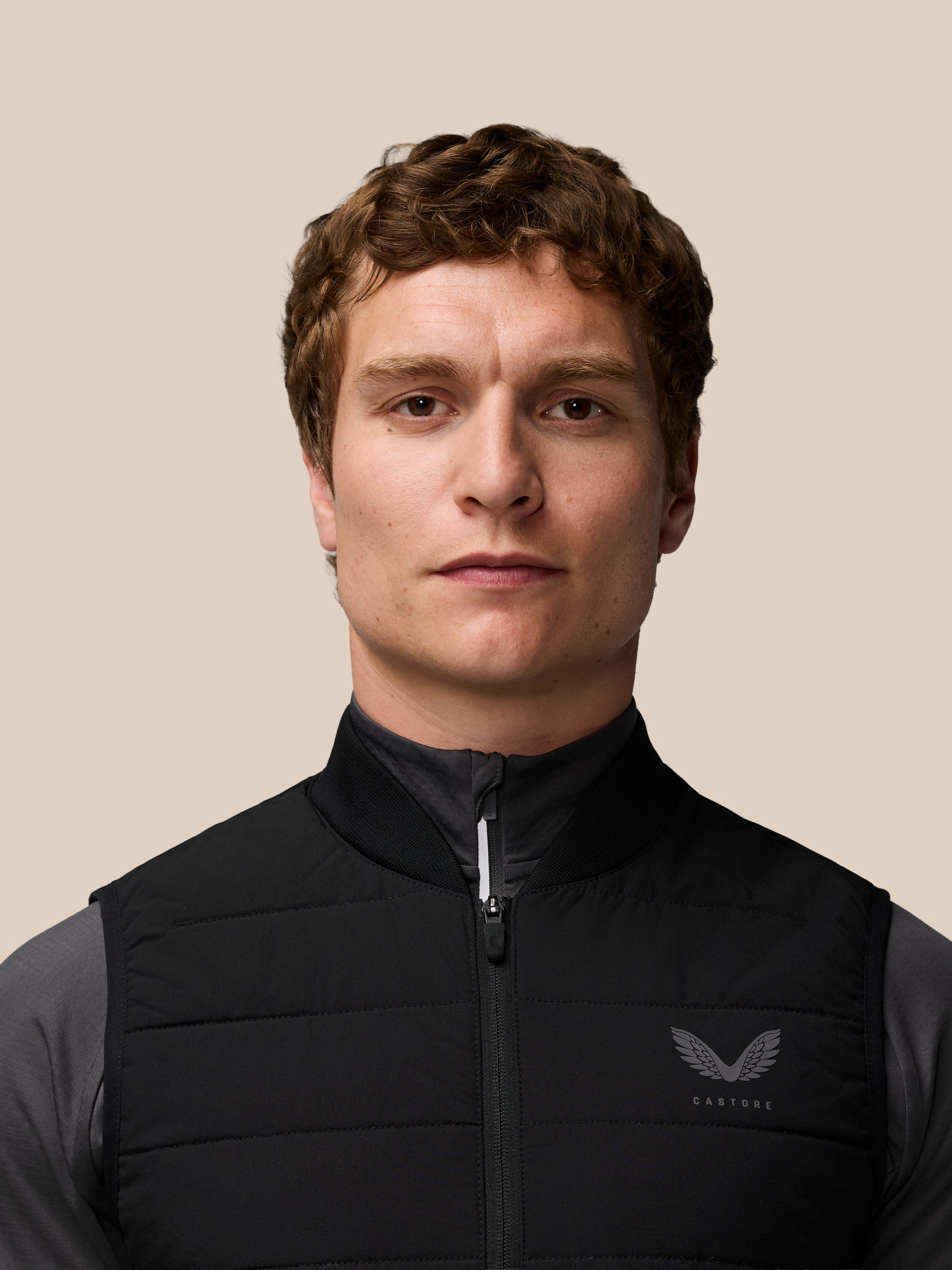 Male model in black sleeveless Apex Training Gilet with zip front and ribbed collar against a beige backdrop.