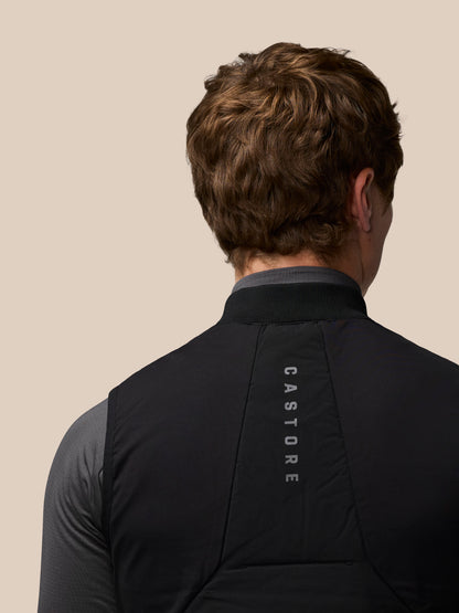 Back view of a man in a black sleeveless Apex Training Gilet over a grey top, beige background with Castore branding down the back