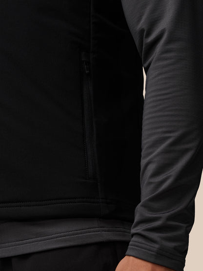 Close-up of black Apex Training Gilet showing a zippered side pocket and ribbed hem, with a gray sleeve visible.