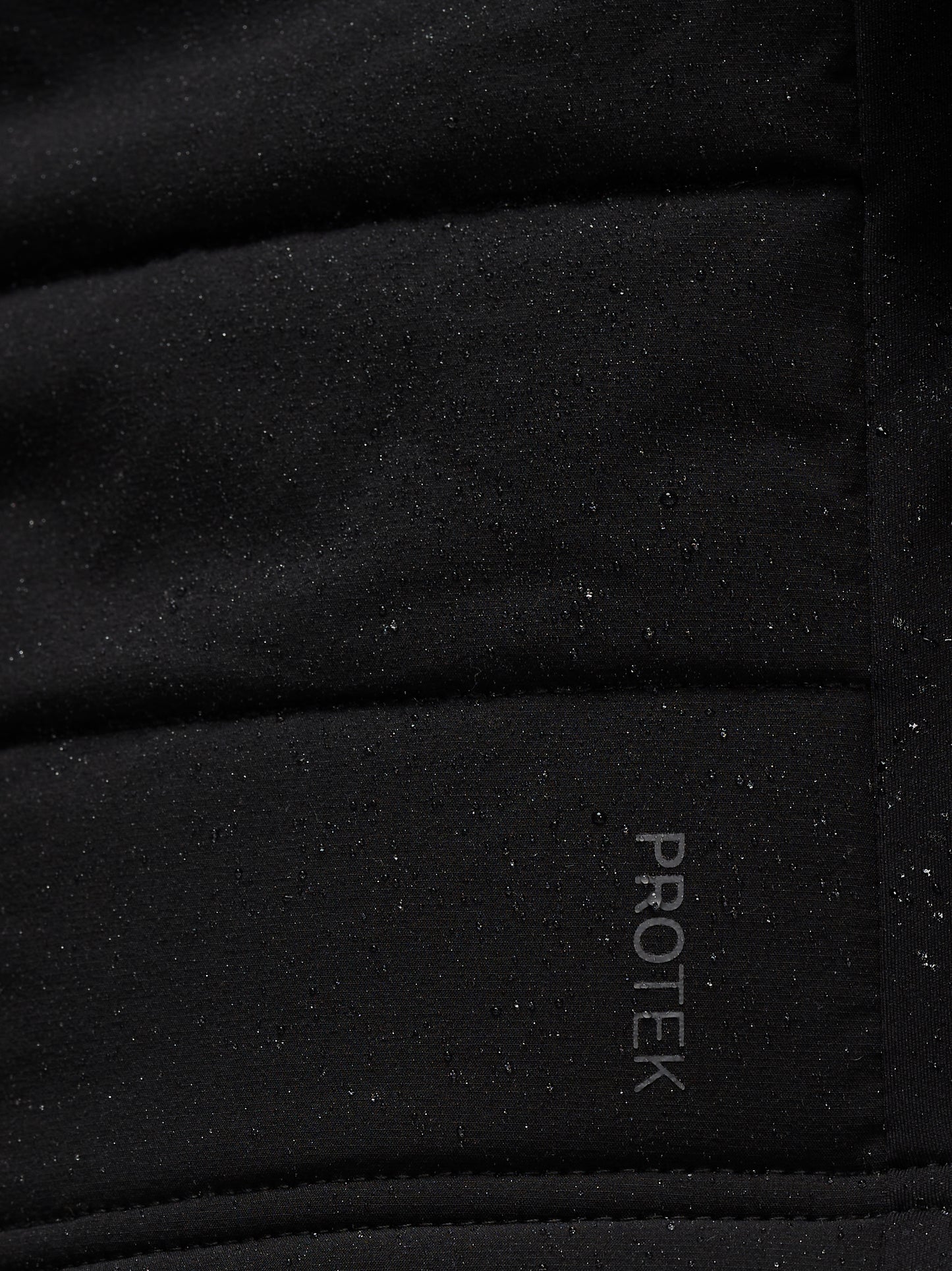 Close-up of black performance fabric with speckled texture and Protek branding on Apex Training Gilet