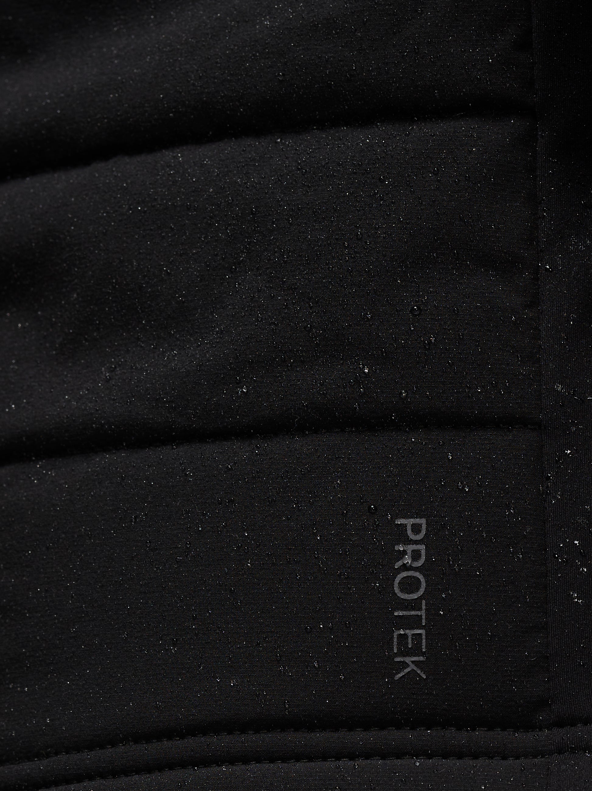 Close-up of black performance fabric with speckled texture and Protek branding on Apex Training Gilet