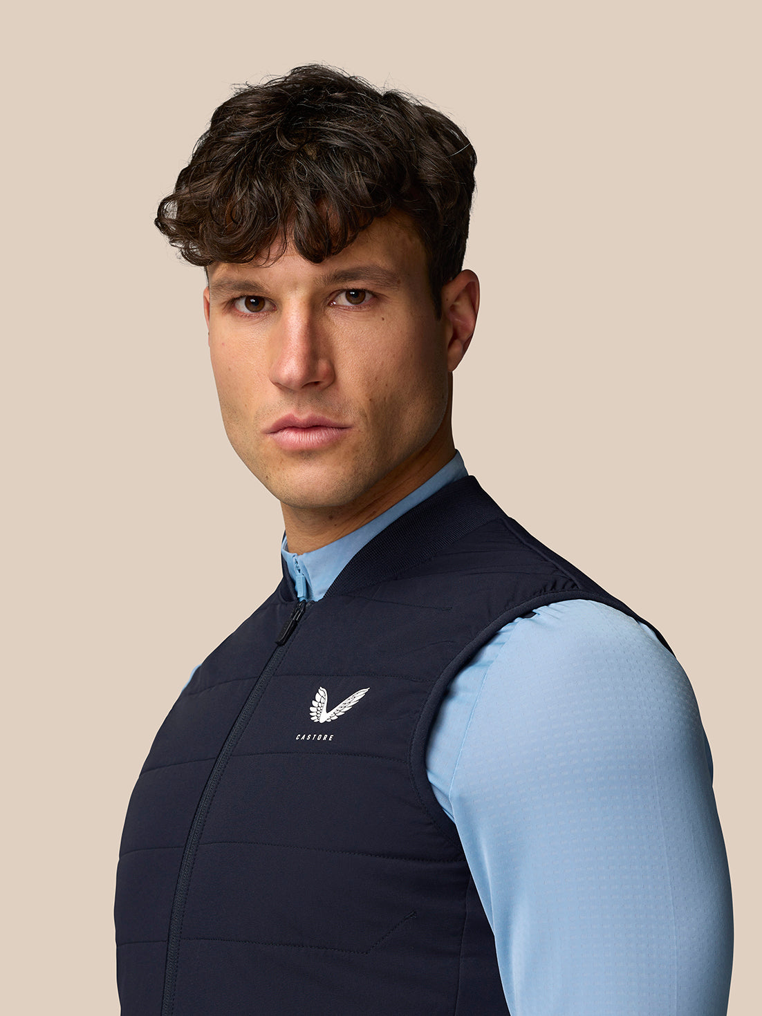 Profile of male model wearing navy Apex Training Gilet with back branding and left chest Castore logo