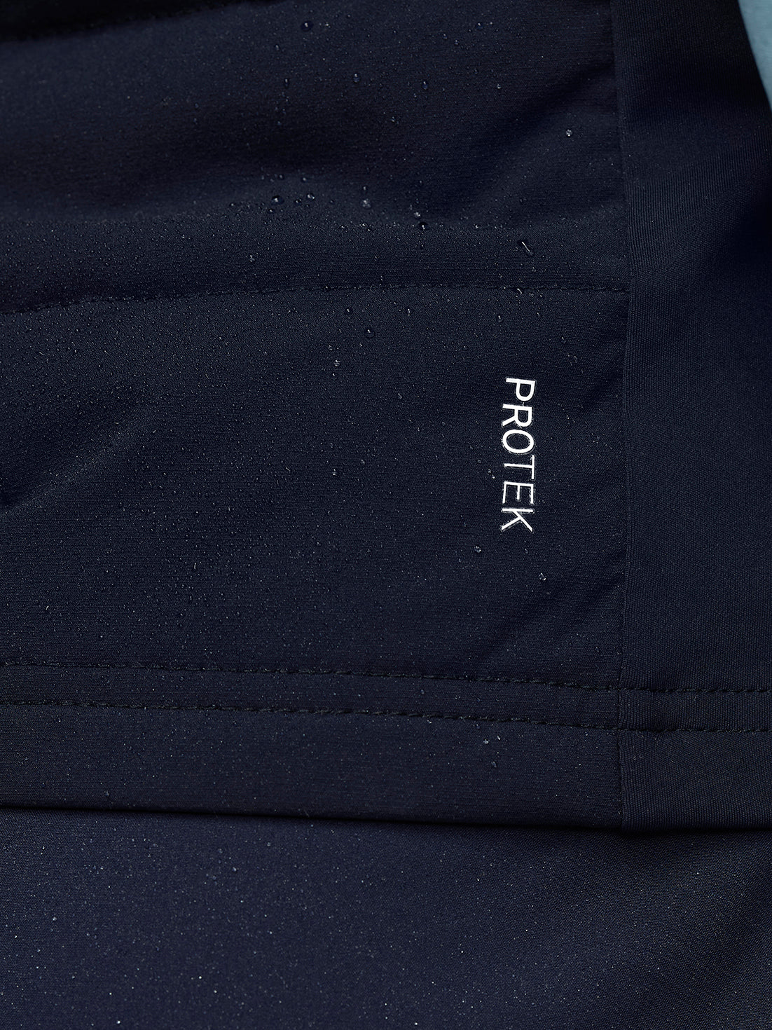 Close-up of navy Apex Training Gilet fabric with a vertical ProTek branding patch.