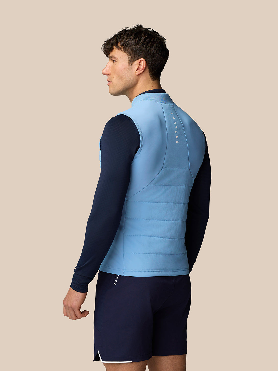 Man in sky blue sleeveless Apex Training Gilet seen from the back with quilted panels and reflective branding