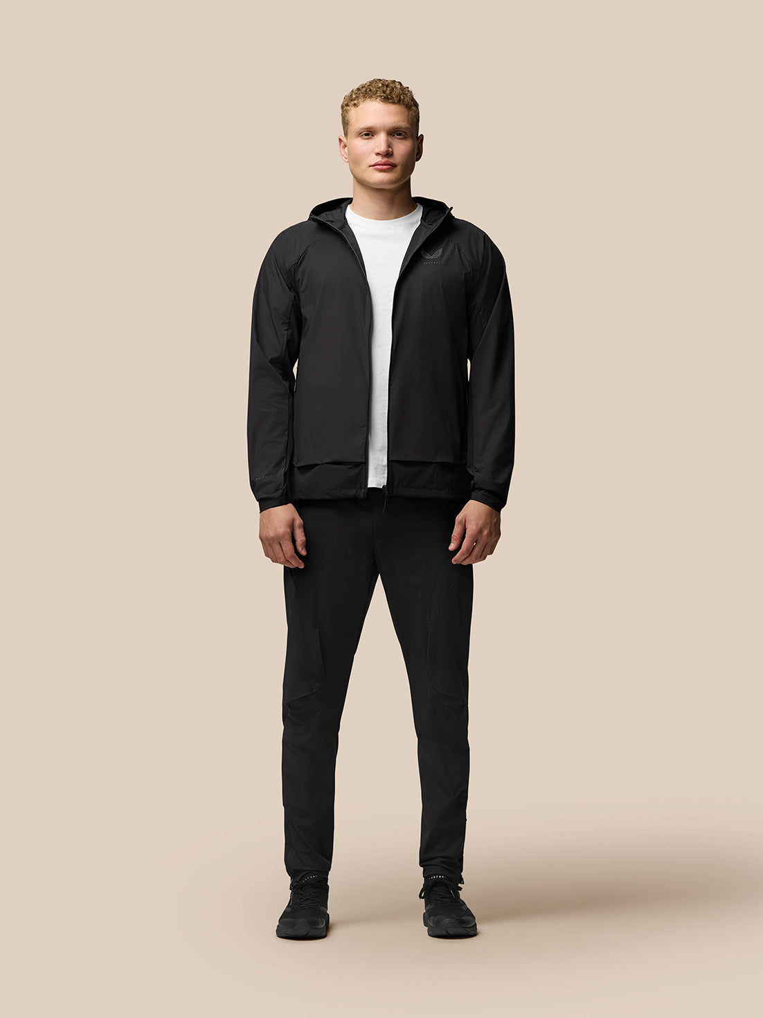 Male model in black Flex Hooded Jacket zipped up with hood down, white T-shirt and cap
