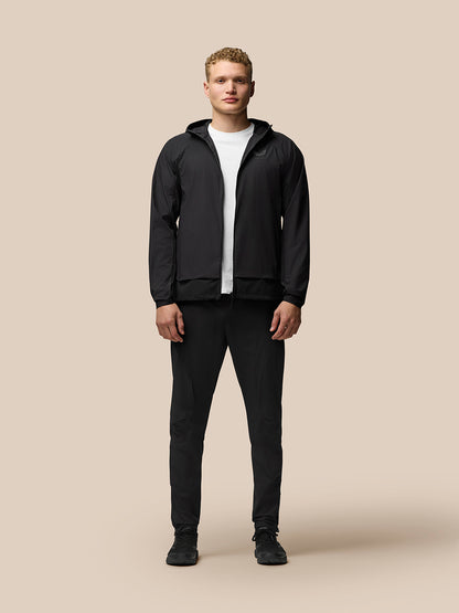 Male model in black Flex Hooded Jacket zipped up with hood down, white T-shirt and cap