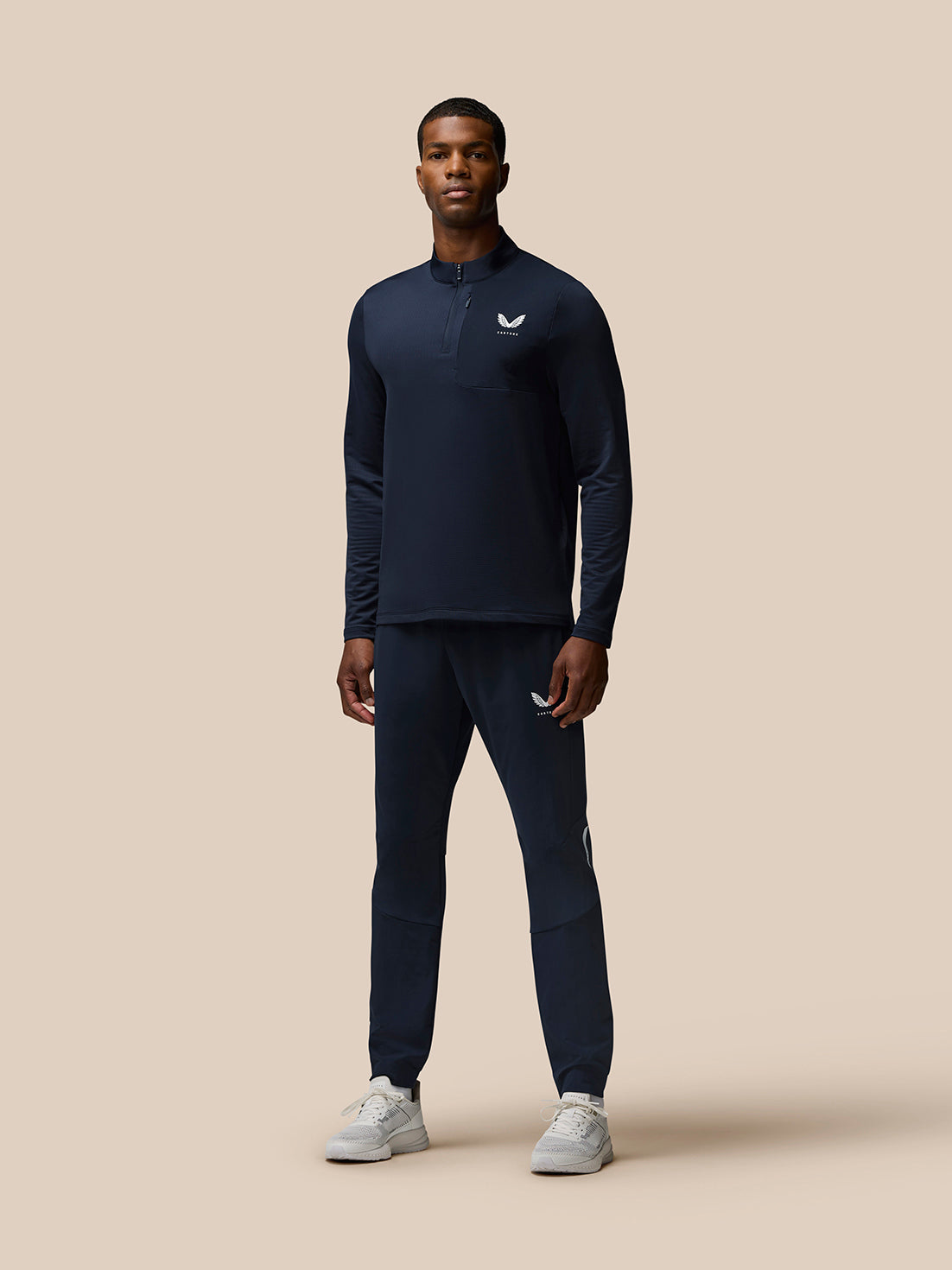 Male model in navy training set with quarter zip top and matching Flow Training Joggers with Castore logos on chest and thigh