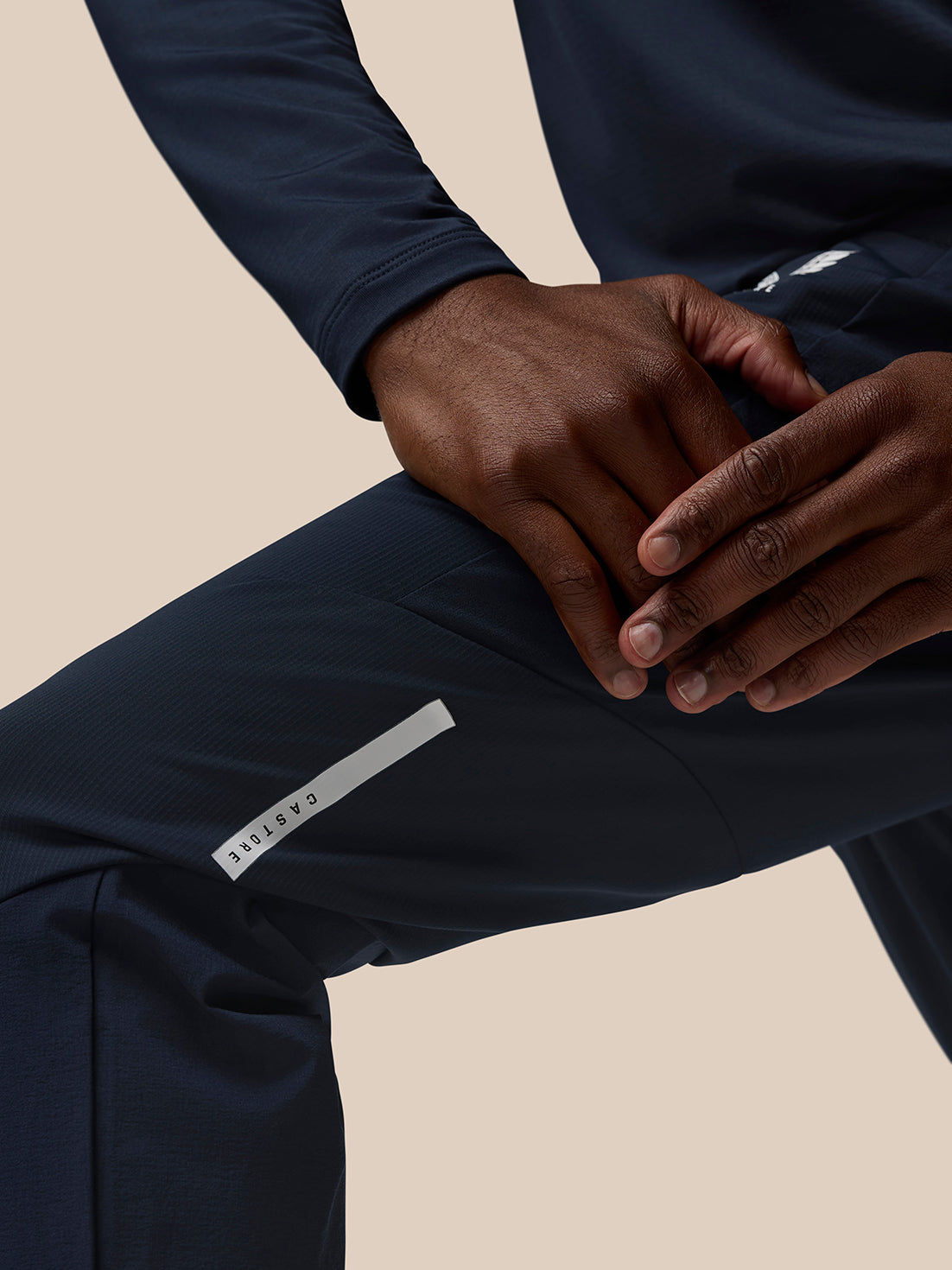 Close up of navy Flow Training Joggers with hands resting on knee and a white Castore label on the thigh pocket