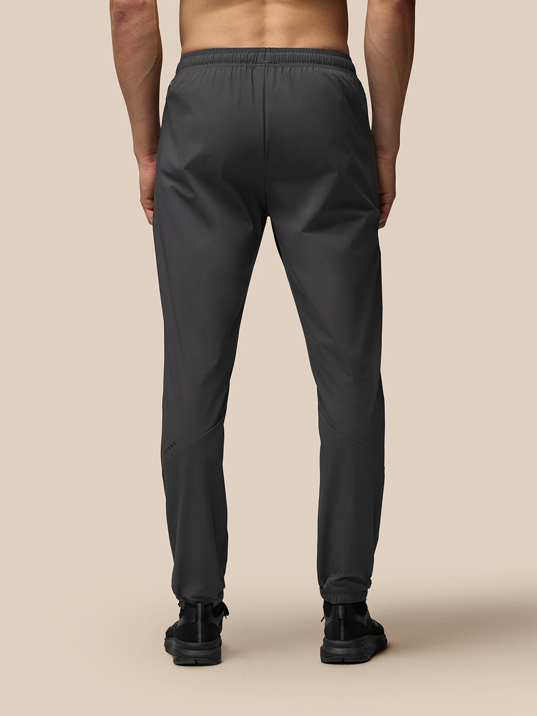 Back view of a man wearing dark grey lightweight flex joggers with an elastic waistband and left leg branding.