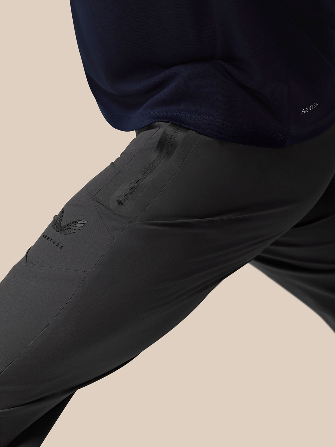 Close up of a jogger leg with a zip pocket and a wing badge on dark fabric.