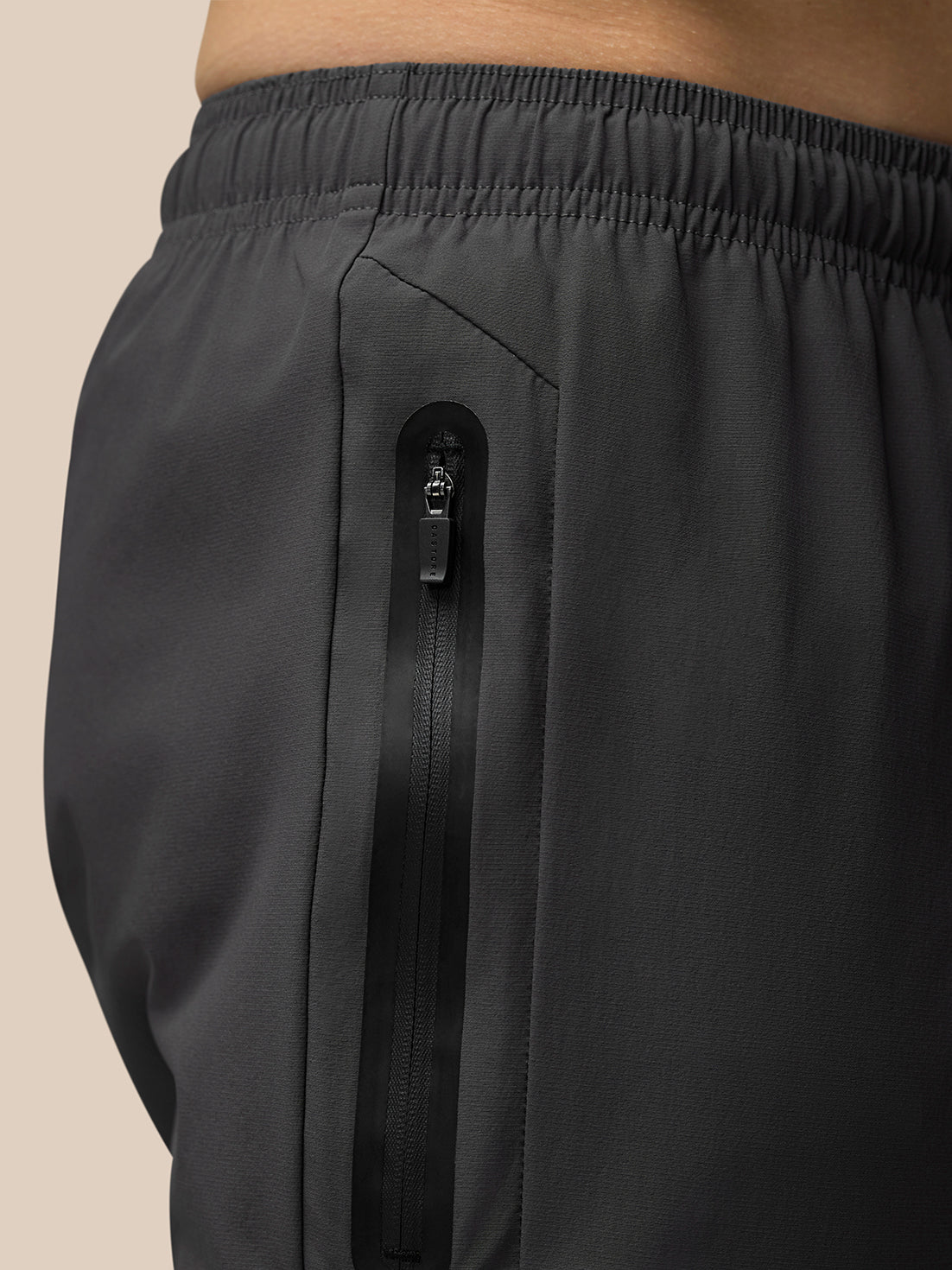 Close up of dark grey flex joggers showing a vertical hip zip pocket.