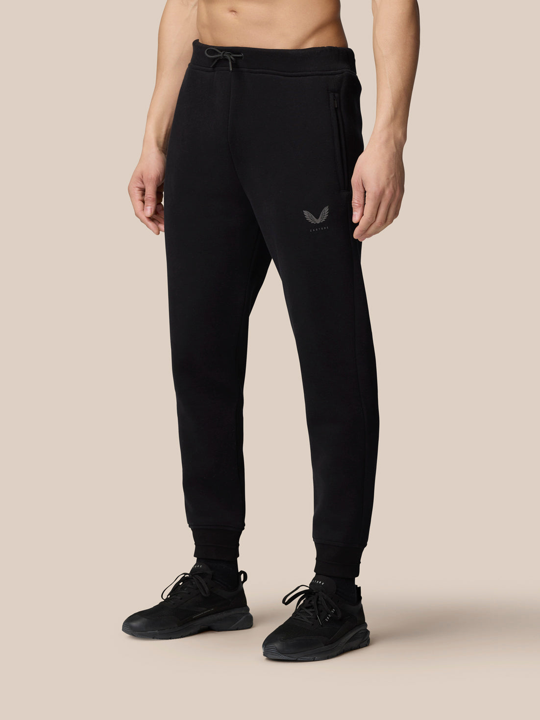 Lower body shot of a man in black Adapt Fleece Joggers showing a small logo on the thigh and tapered legs