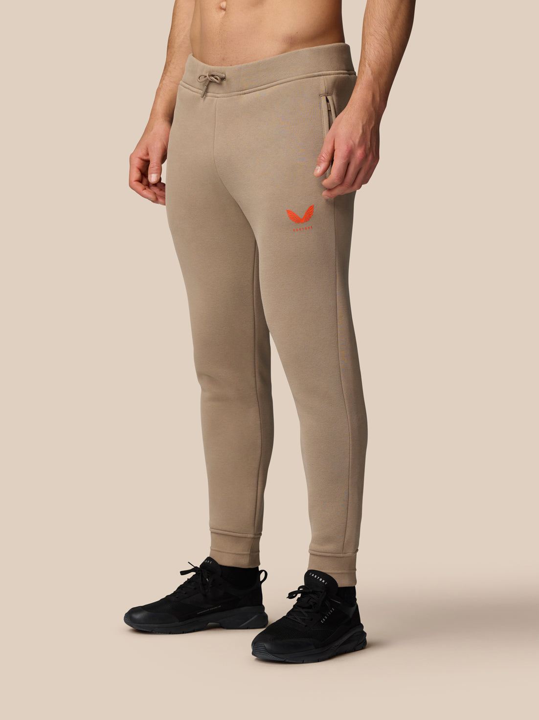 Side view of clay Adapt Fleece Joggers on a model highlighting the drawcord waistband and tapered legs.