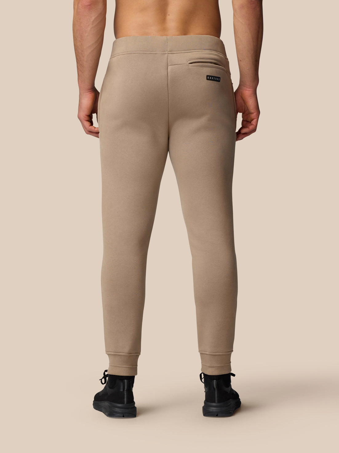 Back view of clay Adapt Fleece Joggers highlighting the thigh logo and cuffed ankles.