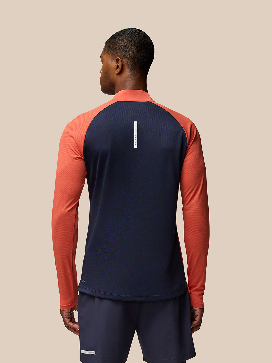 Back view of a model wearing a Breathable 1/4 Zip in navy with orange sleeves.