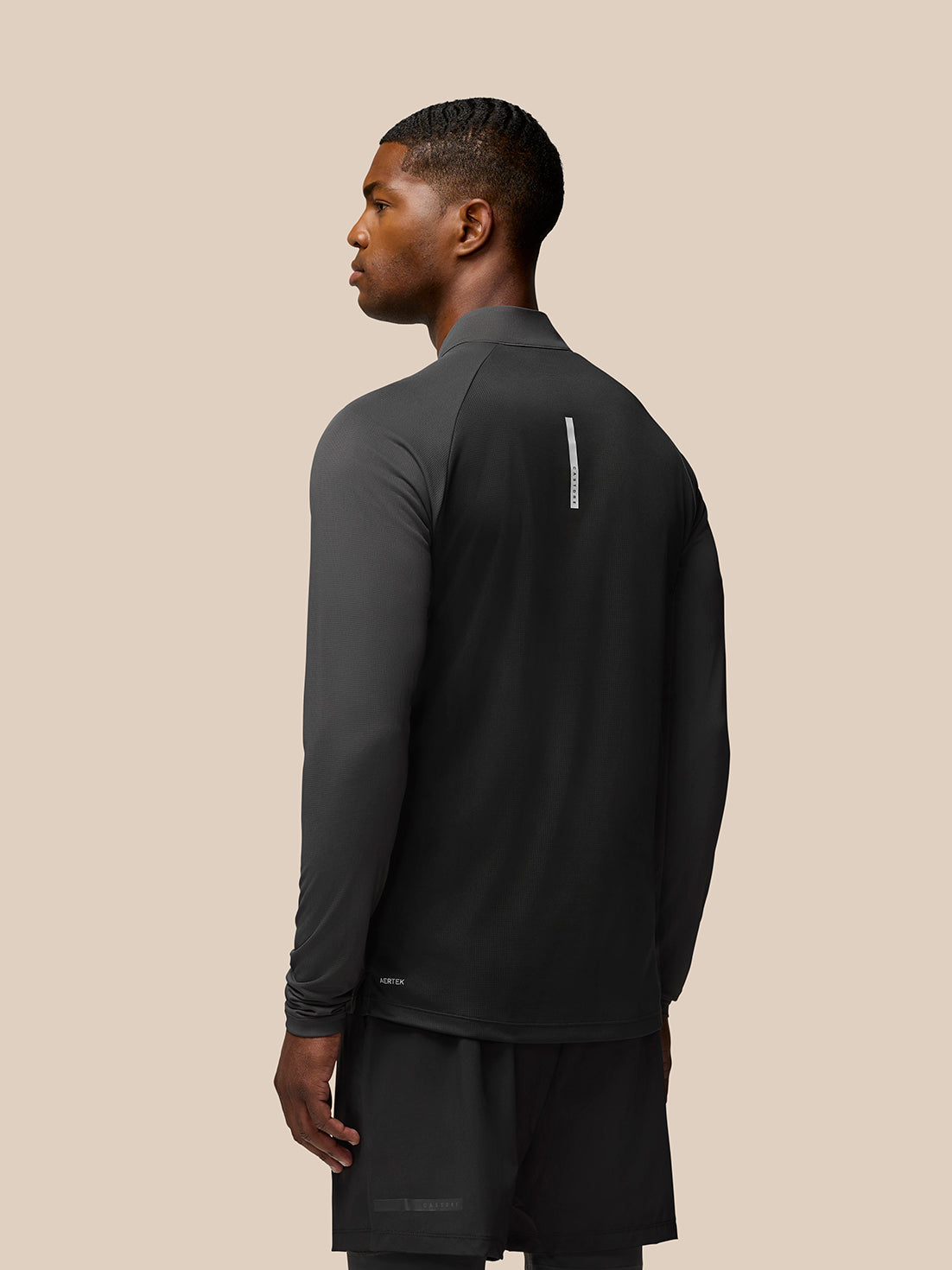 Back view of man in gunmetal Flow Training long sleeve top with vertical Aertek stripe along the back.