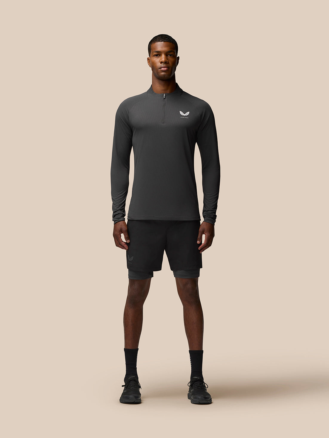 Full-body shot of a man wearing a gunmetal Flow Training quarter-zip top with black shorts