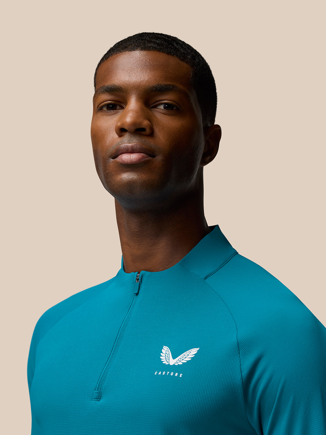 Close up of man wearing Flow Training top in dark aqua with front zip and Castore logo on left chest