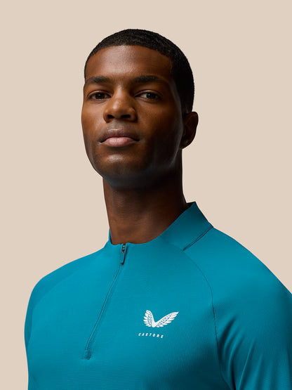 Close up of man wearing Flow Training top in dark aqua with front zip and Castore logo on left chest