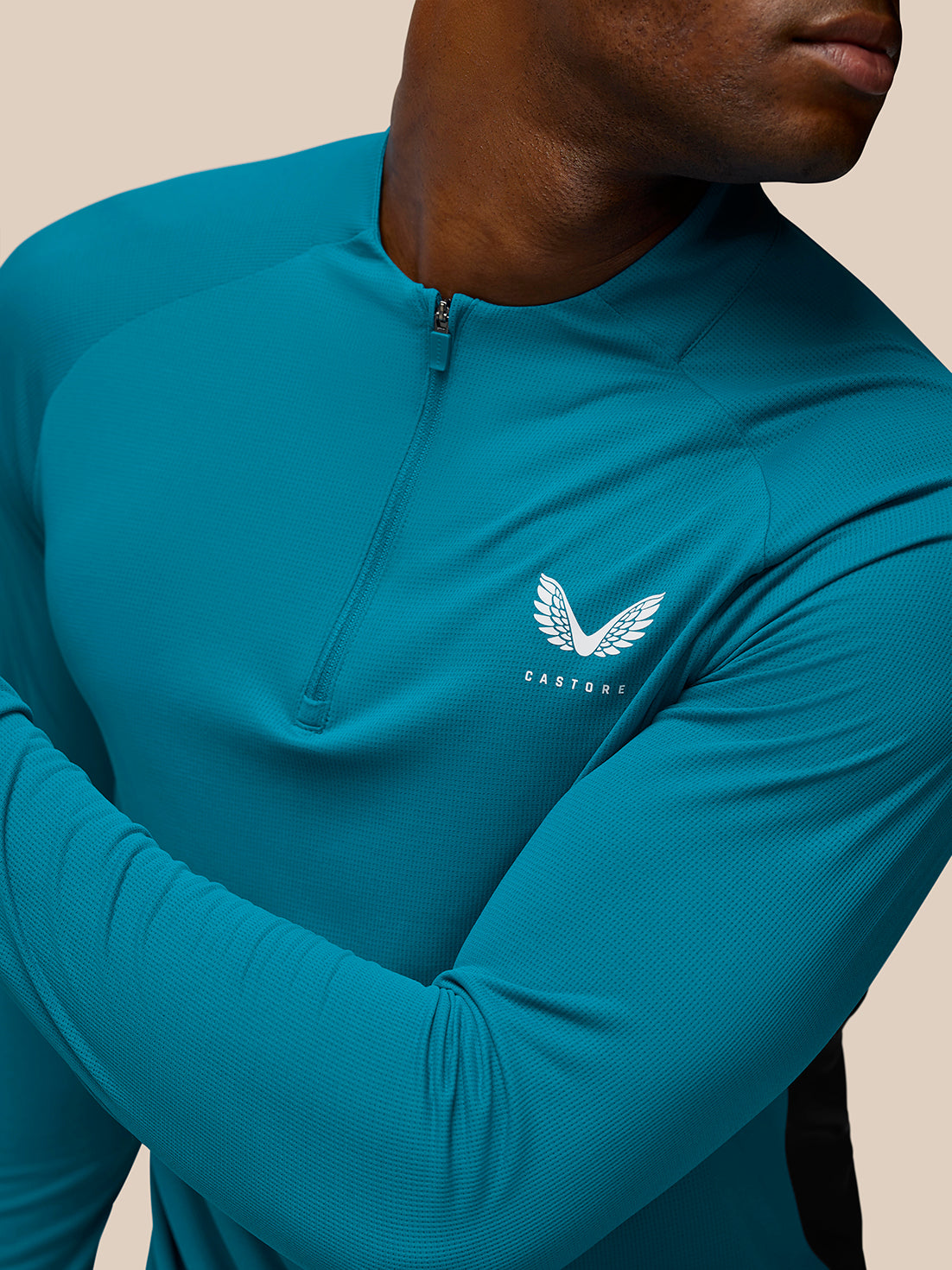 Side angle of model in teal Flow Training top with quarter zip and Castore logo on left chest