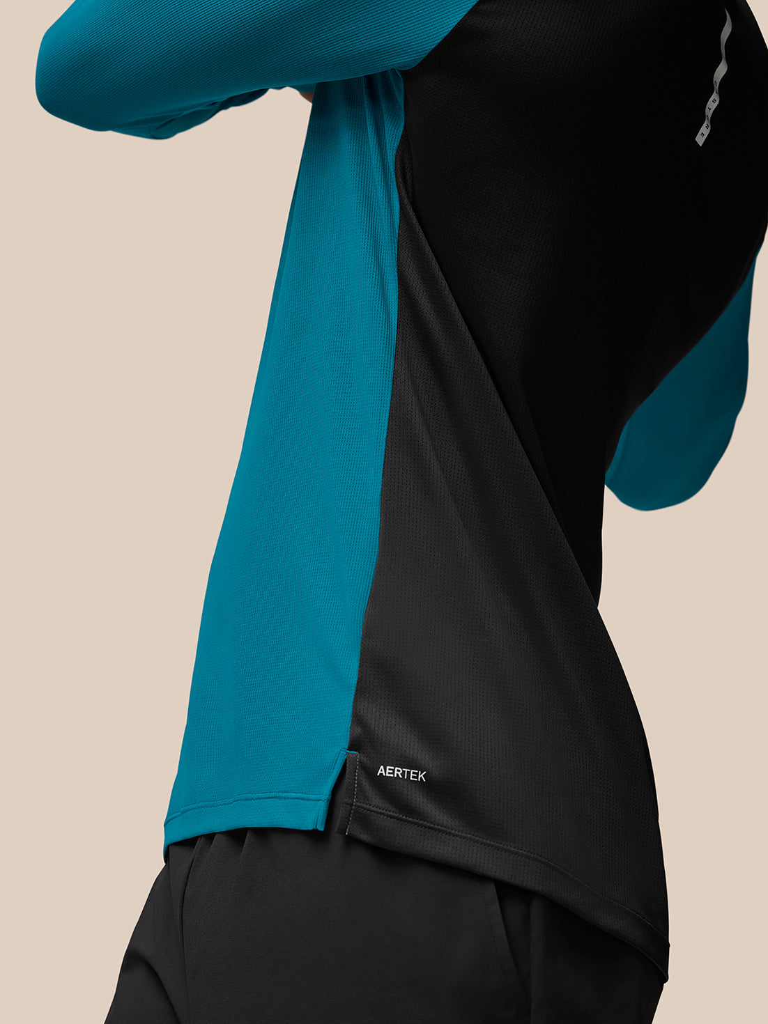 Close-up side view of dark aqua Flow Training top with teal side panels and black back, Aertek branding at hem