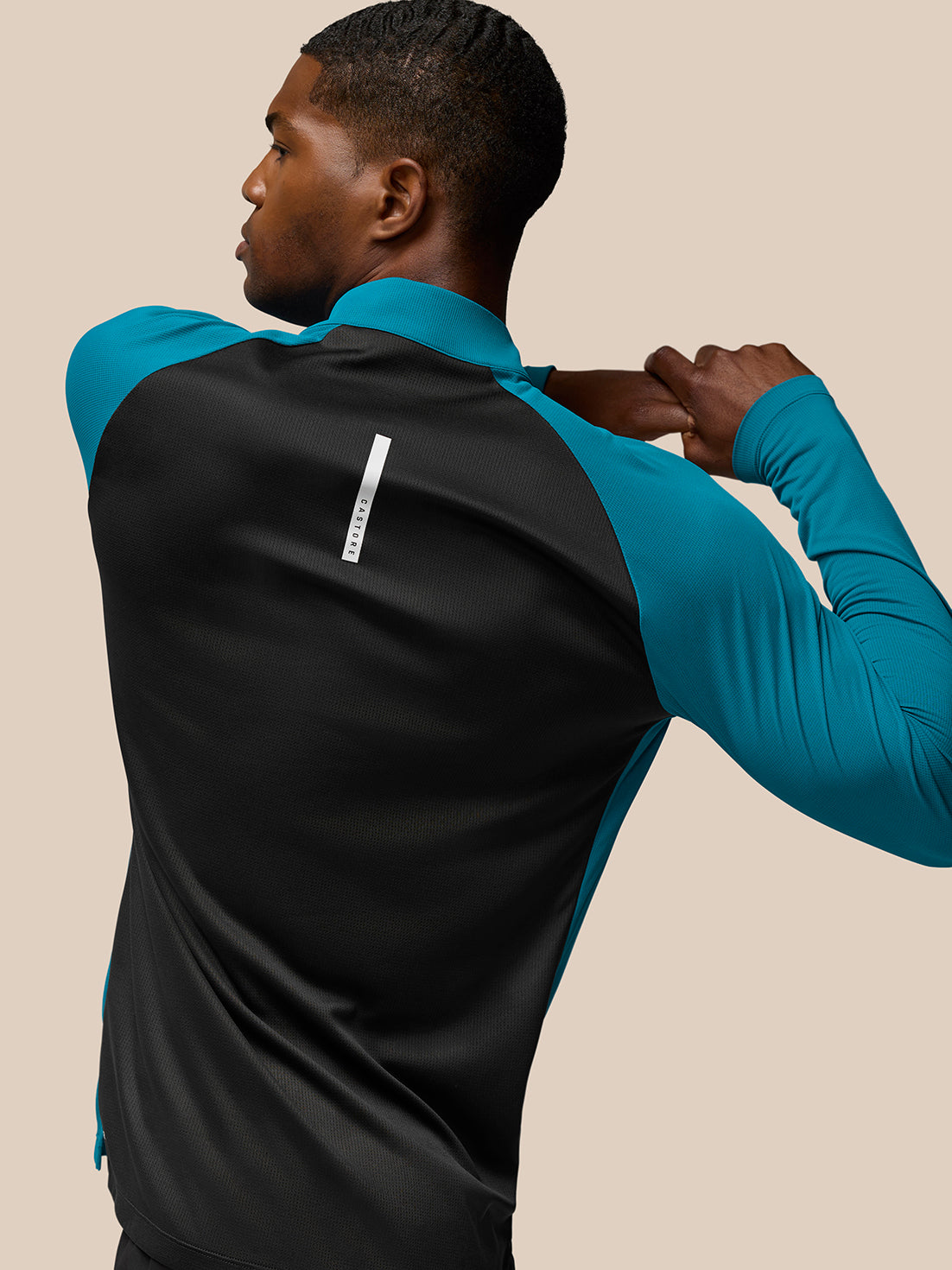 Back view of model wearing Flow Training top with teal sleeves and black back panel and white Castore logo on upper back