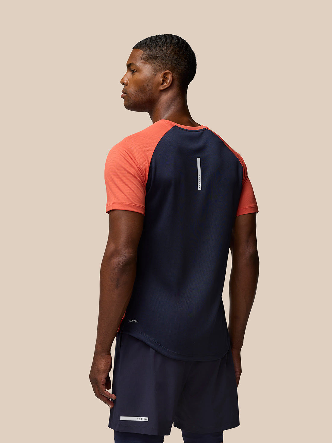 Back view of a man wearing a navy breathable gym T shirt with orange sleeves and a slim white vertical logo on the back.
