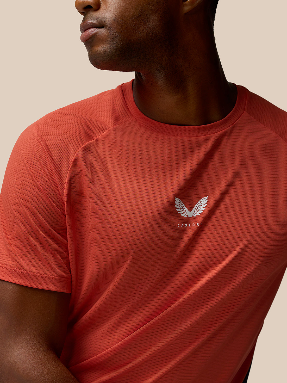 Close up of the chest area of the orange and navy breathable gym T shirt, showing a small white winged logo.