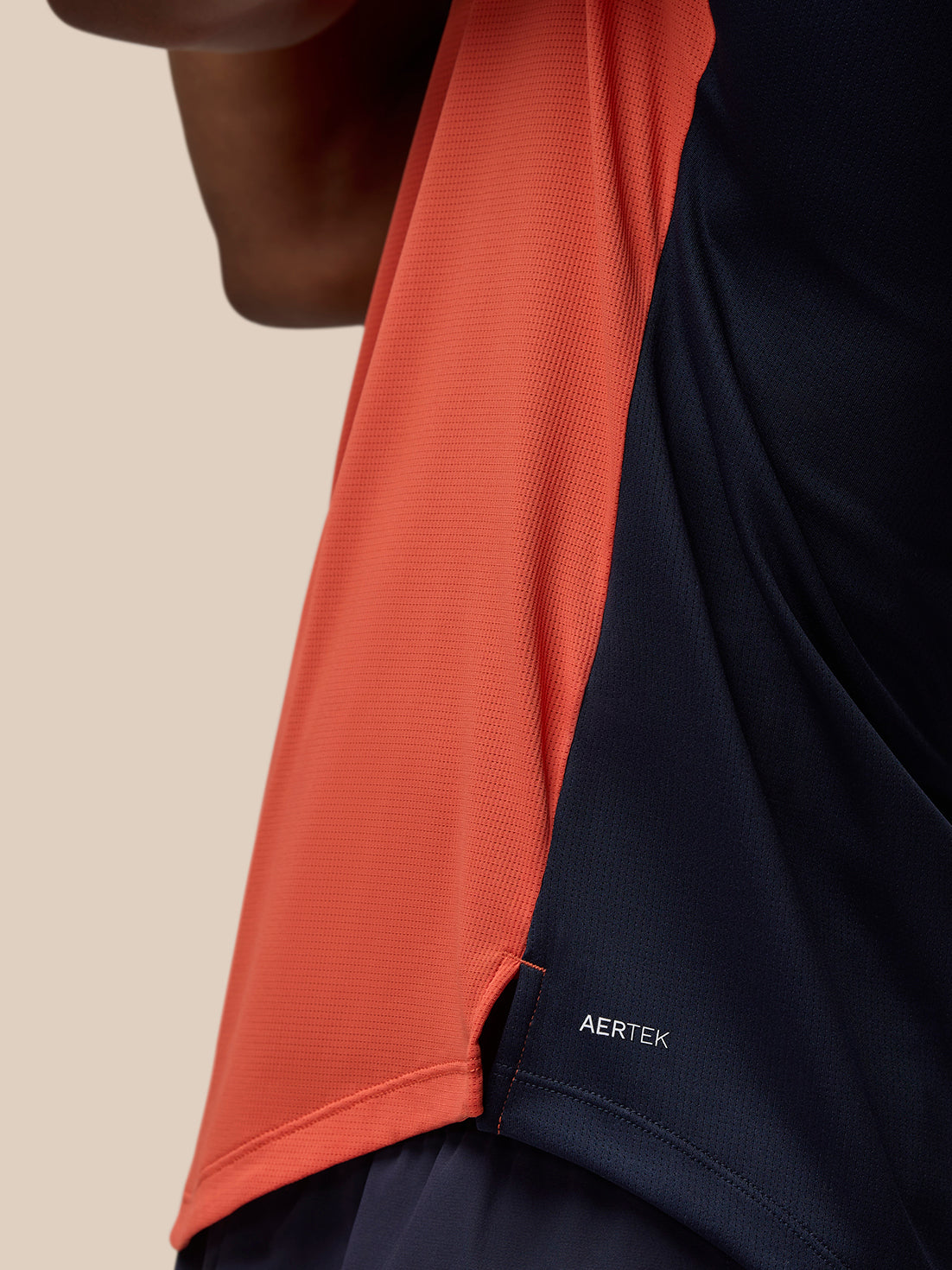 Close up of the orange breathable gym T shirt with navy panel and AERTEK branding at the hem.