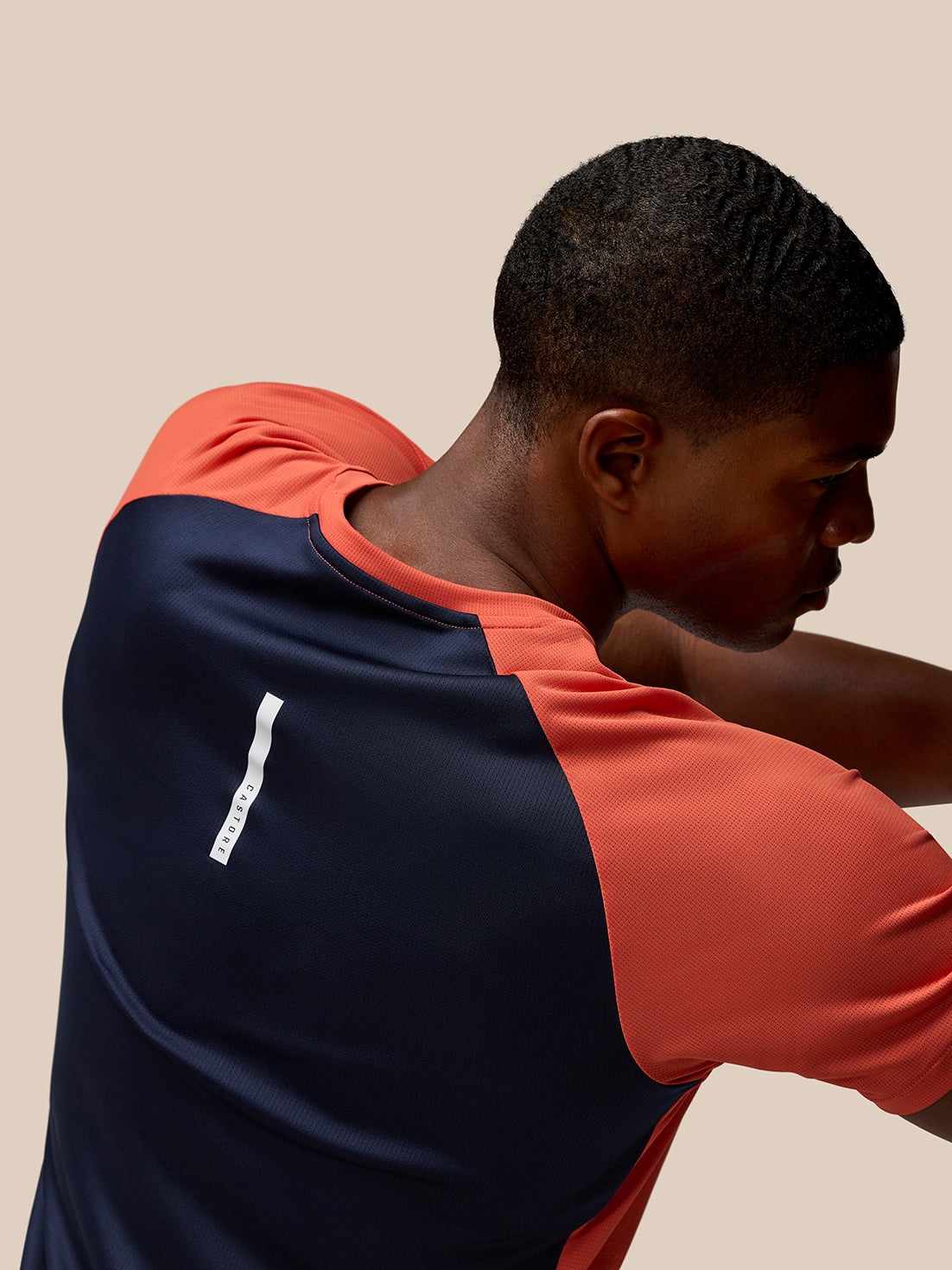 Back view of a model wearing a two tone orange and navy breathable gym T shirt