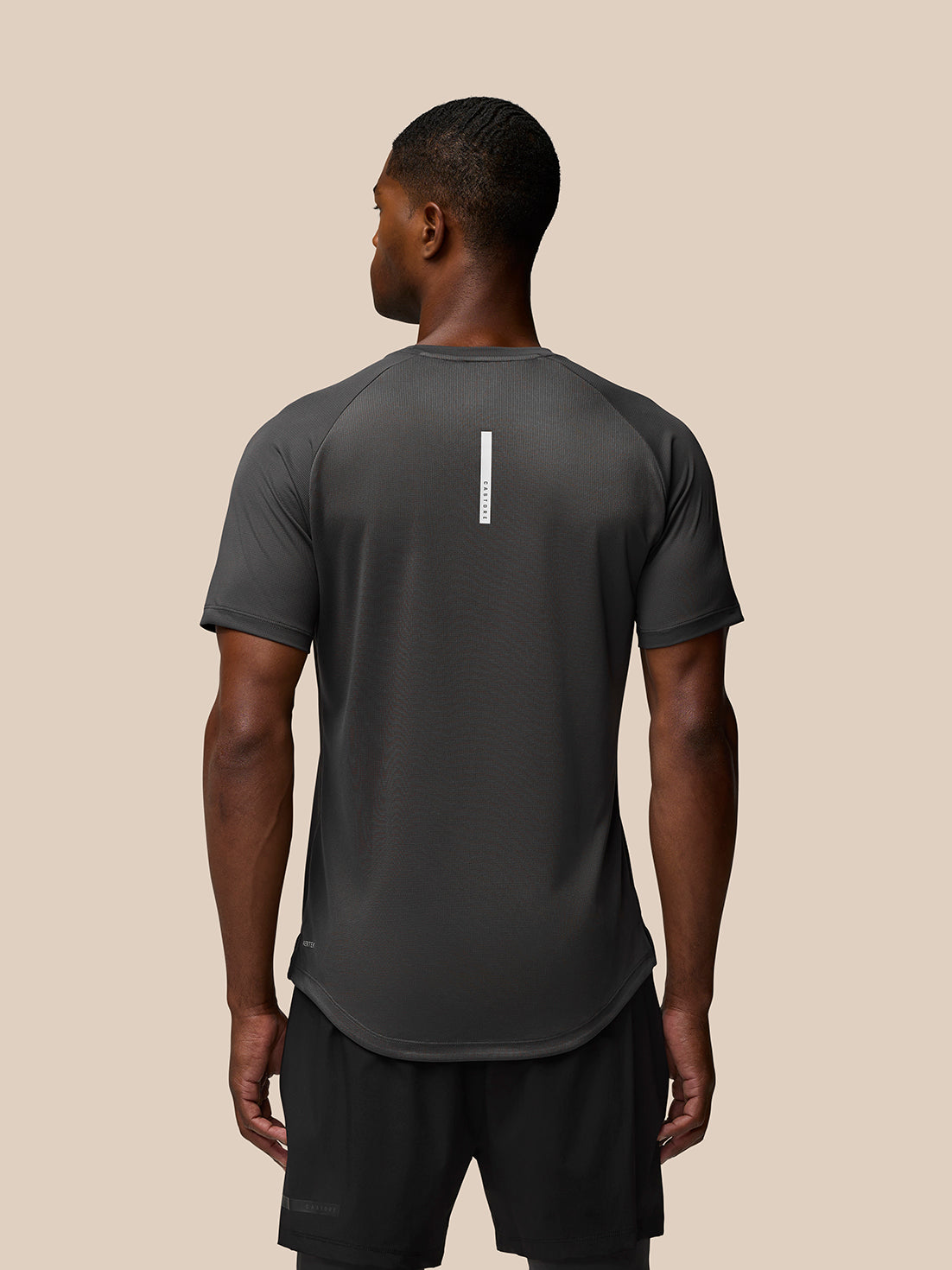 Back view of a man wearing a charcoal Flow Training T-Shirt with a vertical white branding stripe down the center back