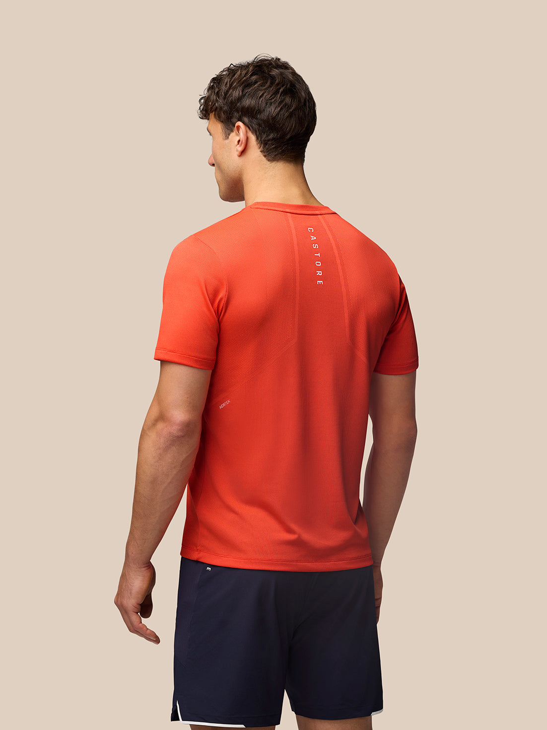 Back view of a man in red Apex Engineered Knit T Shirt with vertical Castore branding down the back