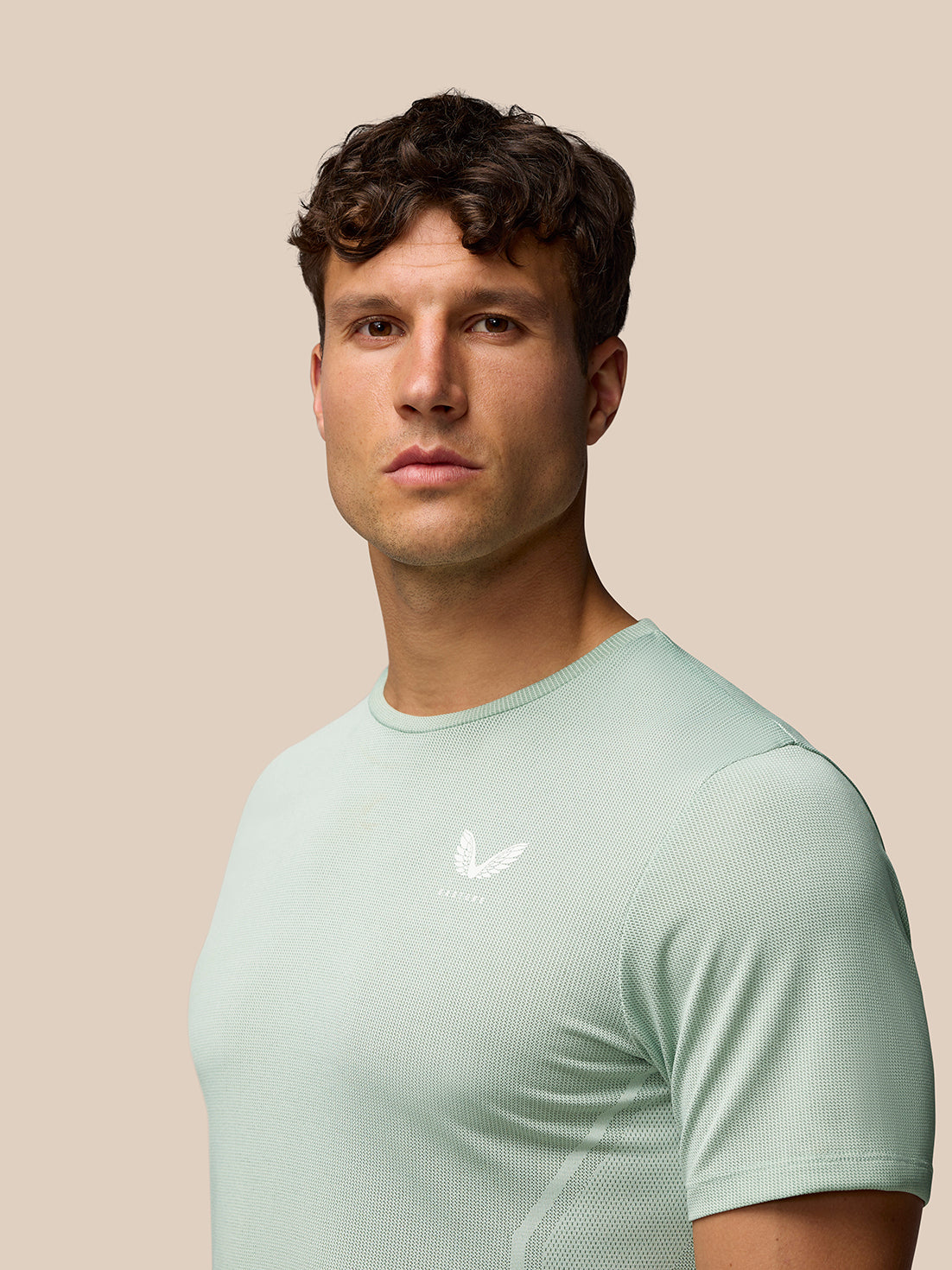 Man wearing mint green Apex Training T Shirt with a white Castore logo on the chest against a beige background.