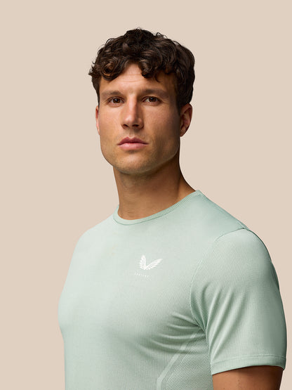 Man wearing mint green Apex Training T Shirt with a white Castore logo on the chest against a beige background.