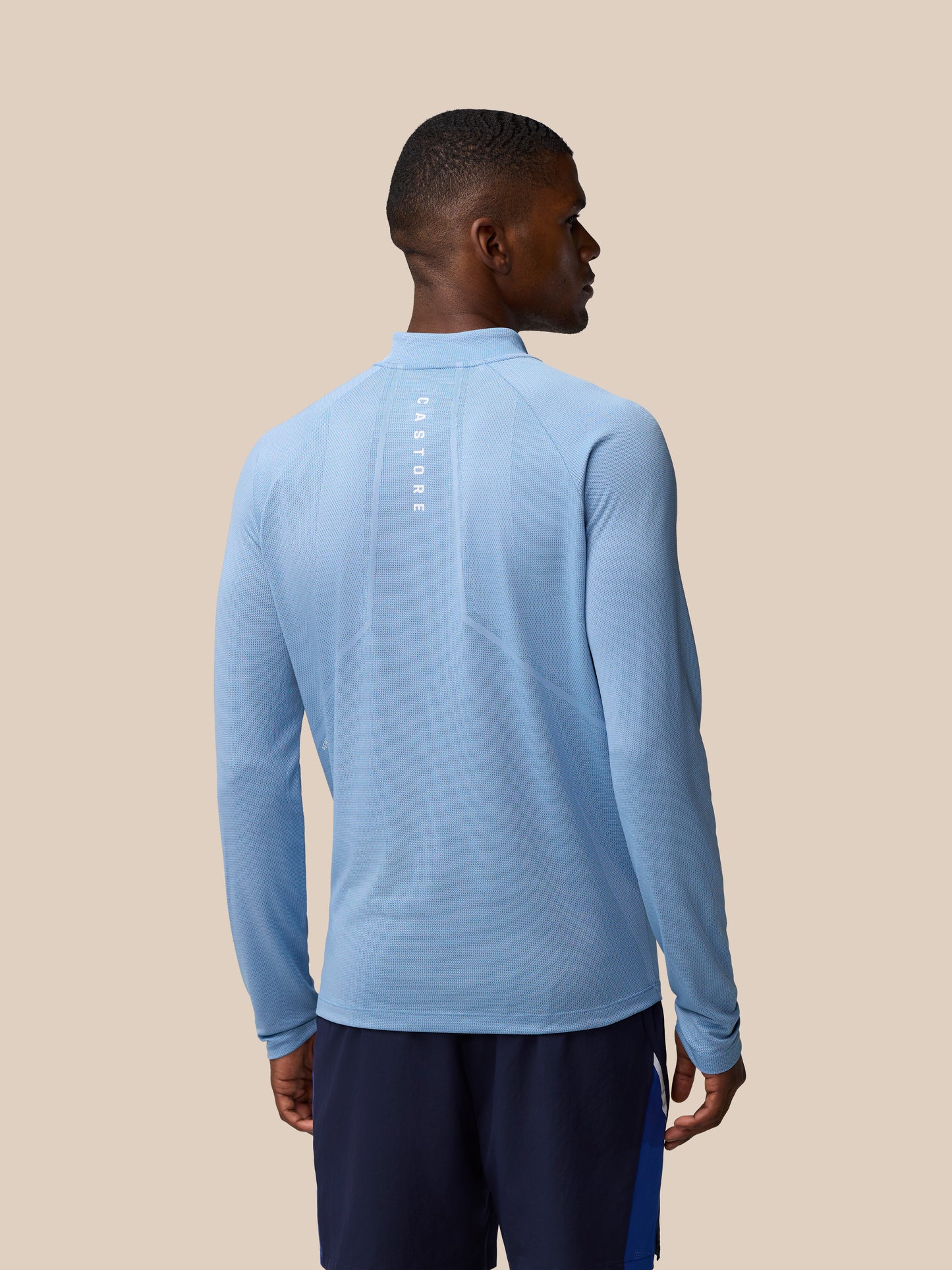 Back view of a man wearing sky blue Apex Training 1/4 Zip Top with reflective branding along the center back.