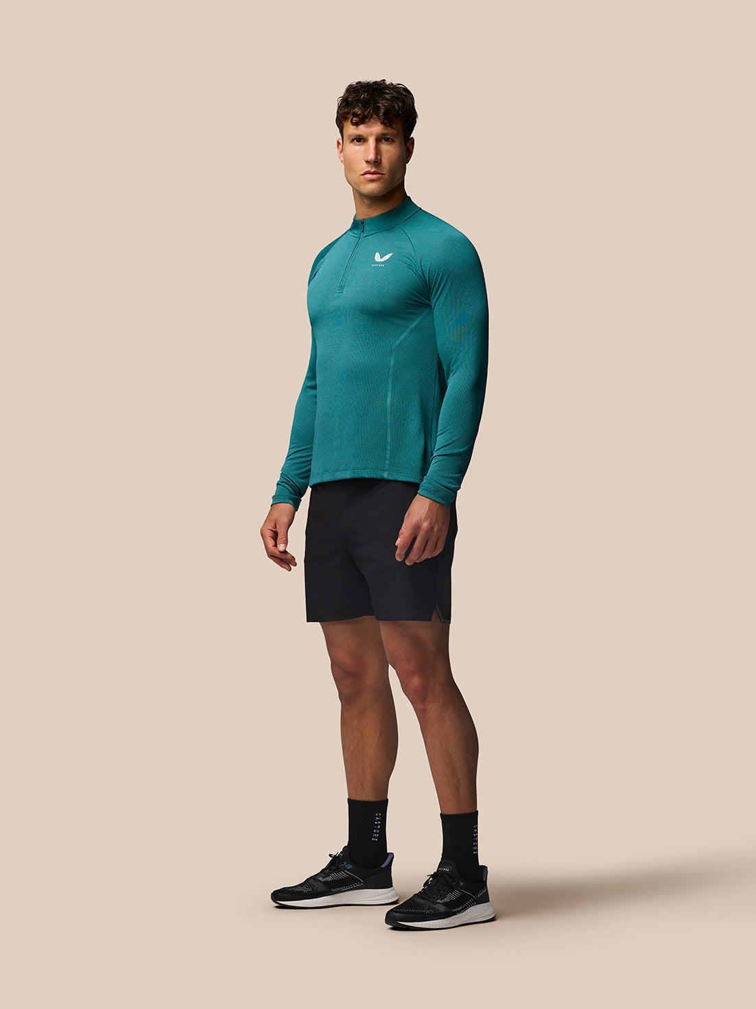Male model wearing aqua Apex Training 1/4 Zip Top with black shorts against a beige background.