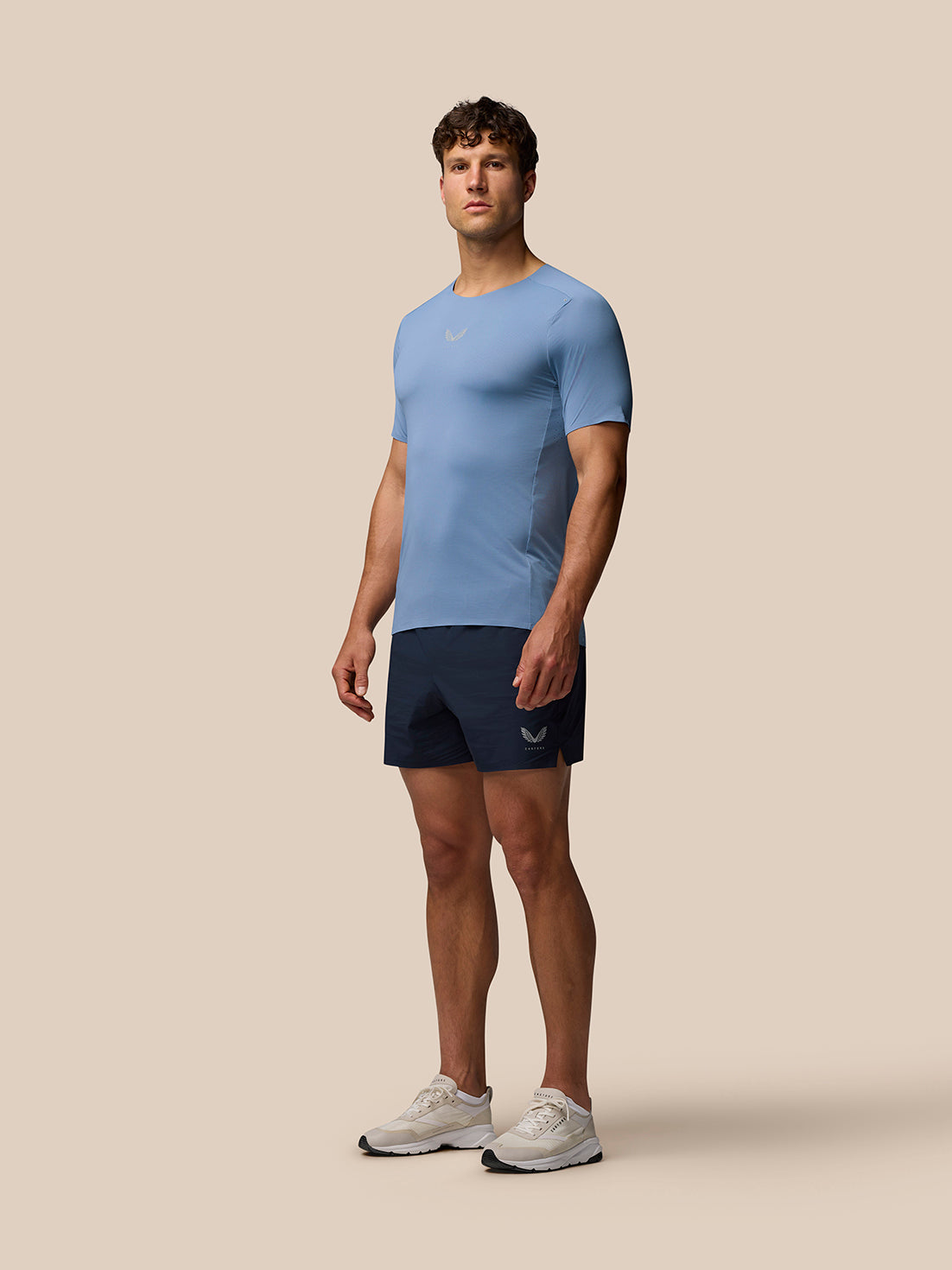 Full-body view of a man in blue Zone Training T-Shirt with navy shorts and sneakers, logos on chest and shorts