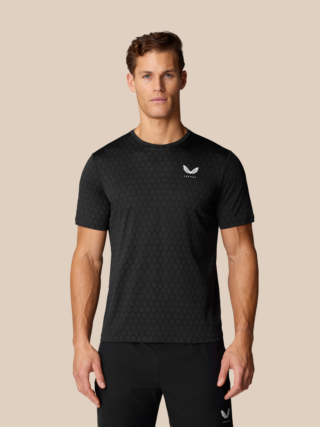 Male model wearing the Flow Training T-Shirt in black with a hexagonal textured pattern and logo on the chest.