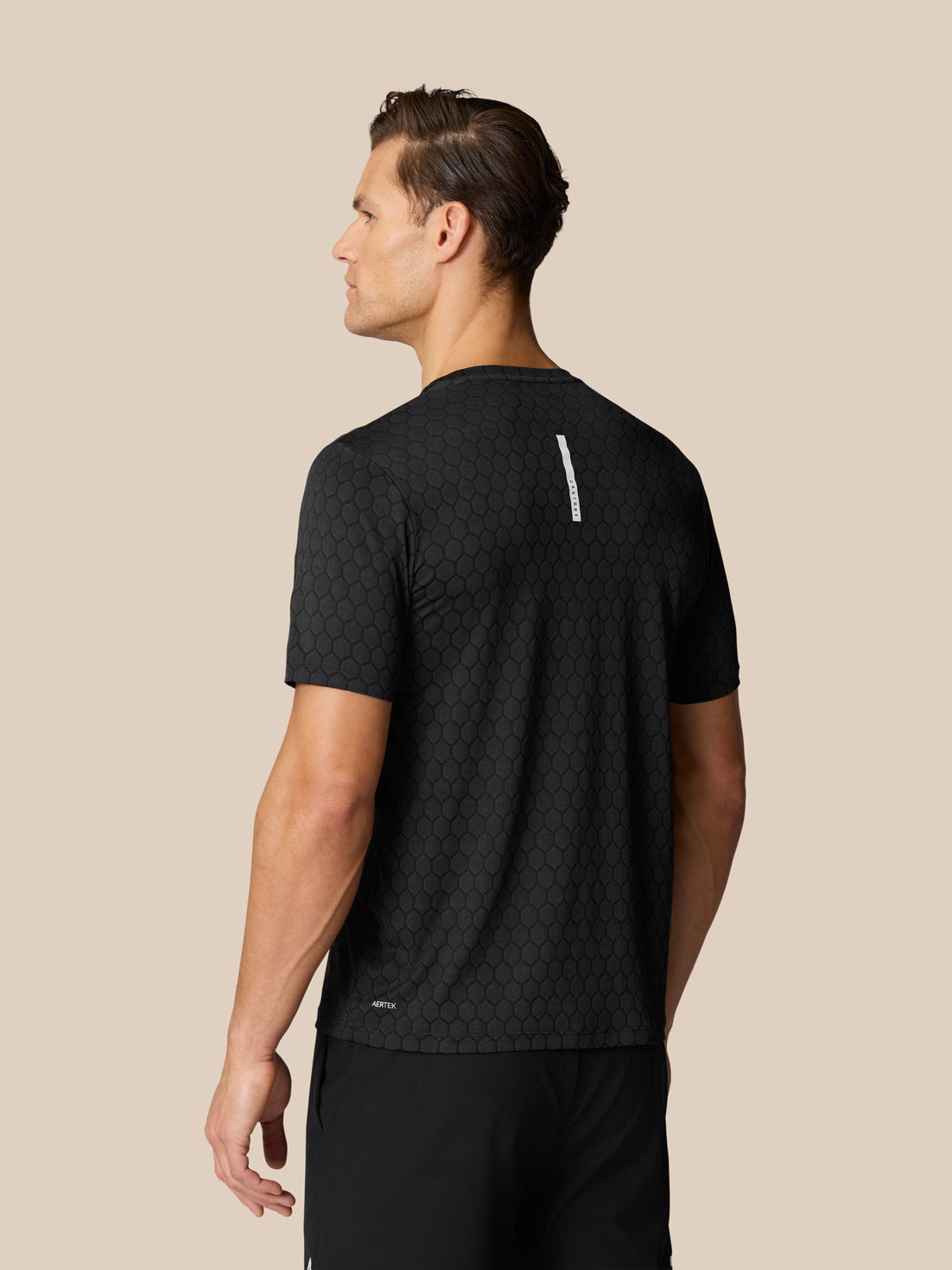Back view of black honeycomb Flow Training T Shirt with vertical white label on upper back