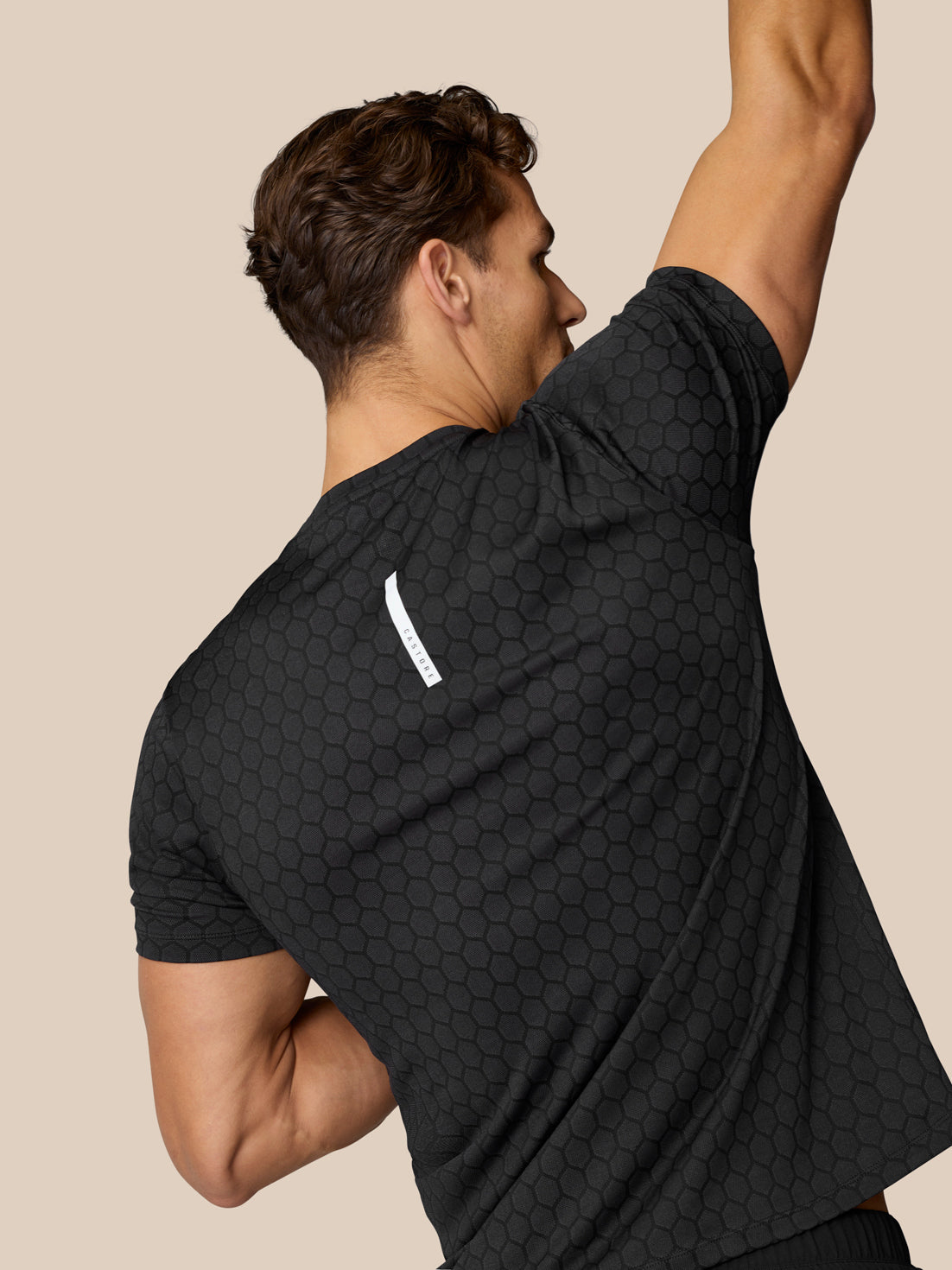 Back view of a male model wearing Flow Training T-Shirt Black with hexagonal knit pattern and a small white label on the shoulder.