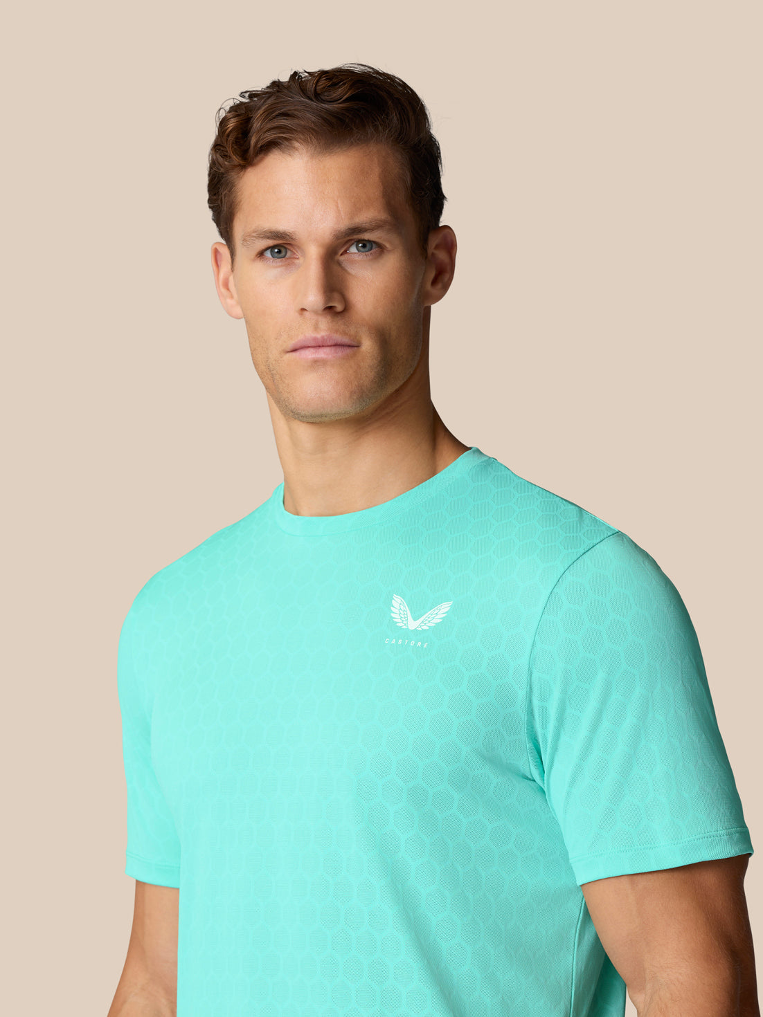 Portrait of a man wearing Flow Training T-Shirt Light Aqua with Castore logo on the chest and hex pattern