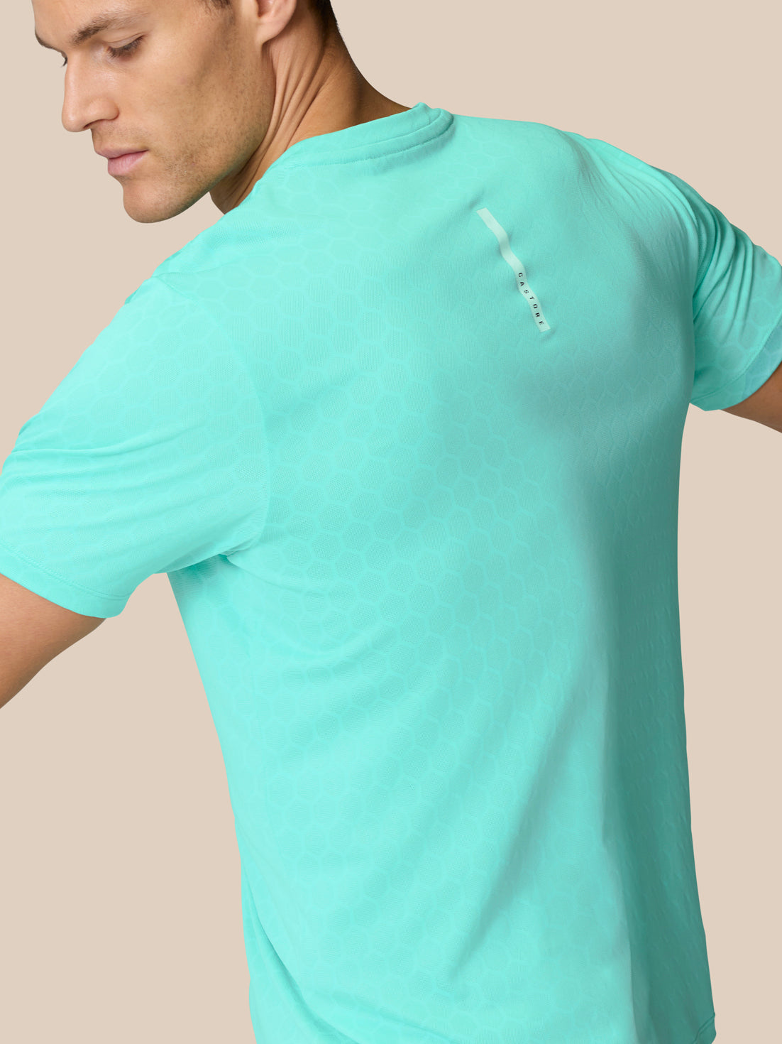 Man wearing Flow Training T Shirt Light Aqua shown from the back with hex knit texture and a vertical branding tag