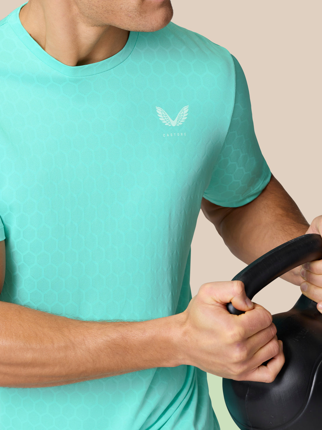 Close up of a man wearing Flow Training T-Shirt in Light Aqua with honeycomb knit texture and Castore logo, gripping a kettlebell
