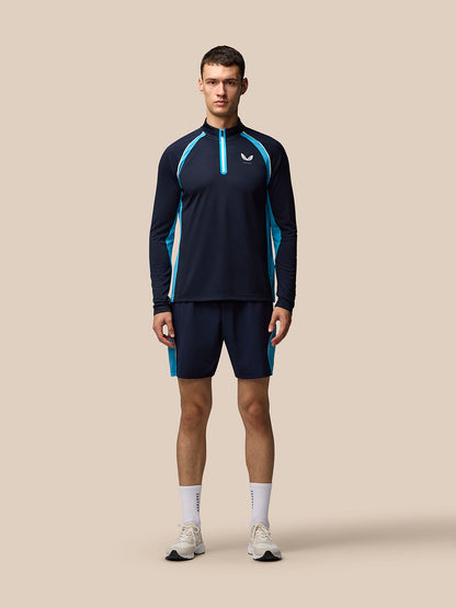 Male model wearing navy tennis long sleeve top with turquoise piping and front quarter zip, Castore logo on the left chest.