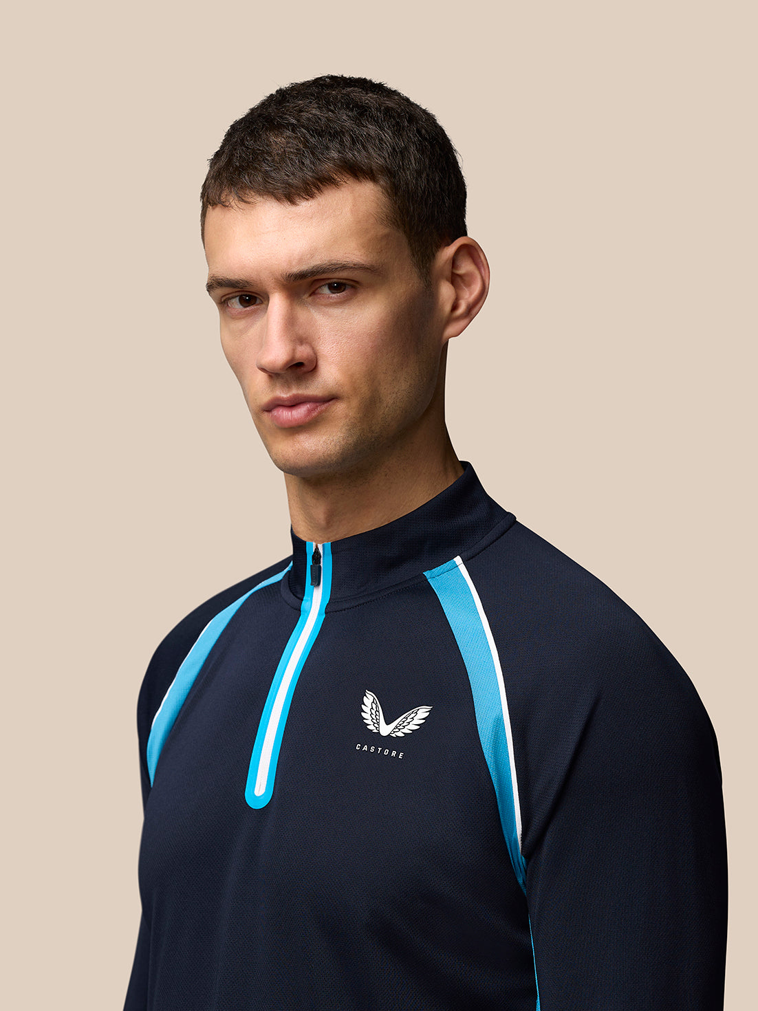 Close up of male model in navy tennis top with blue zip and Castore logo on left chest